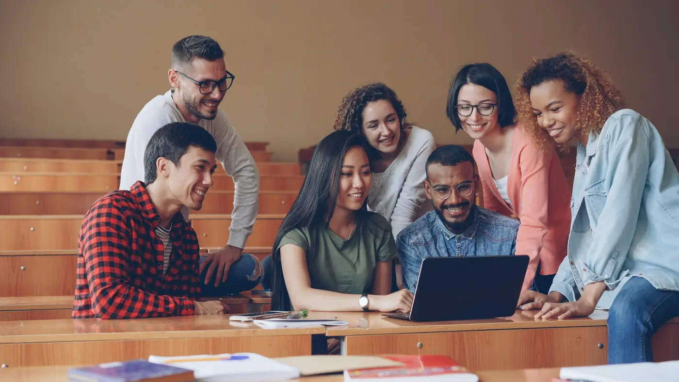 Estudantes reunidos em volta de um notebook numa sala de aula